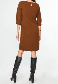 Brun, knälång klänning med 3/4 ärmar och ett nyckelhål i ryggen, tillsammans med släta svarta knähöga stövlar. Slät tyg, figurnära design.