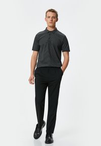 Sort kortærmet polo shirt med diskret mønster, tre-knaps placket, parret med sorte bukser og sorte sko for et strømlinet look.