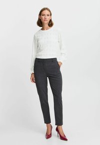 Top bianco a maniche lunghe con design a occhio di pernice e polsini a balze abbinato a pantaloni grigi scuri aderenti e tacchi alti bordeaux.