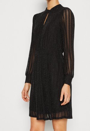 Woman wearing a black long-sleeve dress with vertical sheer stripes and subtle silver shimmer, keyhole neckline, and pleated skirt.