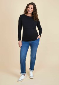 Top negru cu mâneci lungi, cu textură cu nervuri, având un tiv curbat, asociat cu blugi ușor albaștri cu manșete și adidași albi.