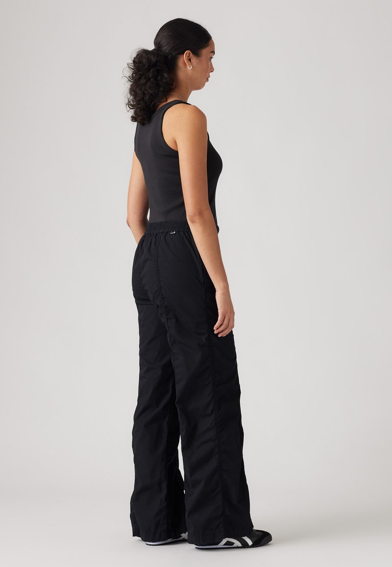 Schwarze, locker sitzende Hose mit elastischem Bund, glatter Textur und ohne sichtbare Muster. Getragen mit einem eng anliegenden schwarzen Tanktop.