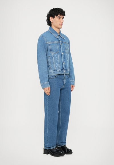 Τζιν μπουφάν και τζιν παντελόνια σε ανοιχτό γαλάζιο, με κοντό σχέδιο, μπροστινές τσέπες και κουμπώματα με κουμπιά, συνδυασμένα με μαύρα chunky παπούτσια.