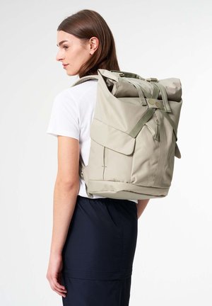 Roll-top backpack in light green fabric with two front pockets, adjustable straps, and contrasting hardware details. Textured finish.