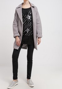 Abrigo gris de gran tamaño con mangas enrolladas, suéter negro de felpa con adornos de estrellas plateadas, jeans ajustados negros y zapatillas plateadas.