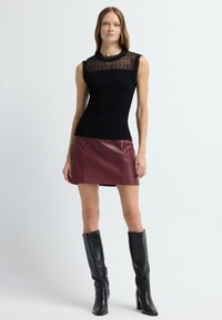 Czarny prążkowany top bez rękawów z przezroczystą wstawką, w połączeniu z bordową mini spódnicą z sztucznej skóry z zamkami z przodu oraz wysokimi czarnymi botkami.