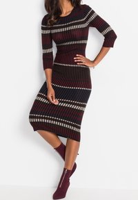 Robe en maille côtelée avec des rayures verticales bordeaux, bleu marine et blanches. Manches trois-quarts, silhouette ajustée et ourlet jusqu'aux genoux.