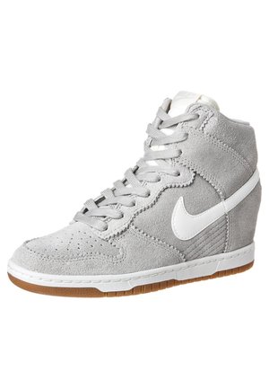 Jasnoszare zamszowe trampki wysokie z białym logo Nike, białą podeszwą środkową, gumową podeszwą zewnętrzną i koturnem.
