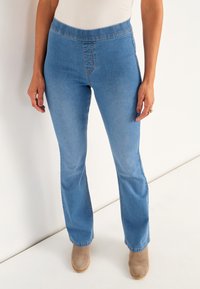 Ljusblå bootcut jeans i denim med medelhög midja, minimal sömnad och en slät yta, i kombination med taupe ankelskålar.