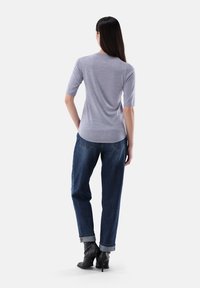 Graues Stricktop mit ¾-Ärmeln, lässiger Passform und rückseitiger Nahtdetails, kombiniert mit hochgeschnittenen, umgeschlagenen dunkelblauen Jeans und schwarzen hohen Stiefeln.