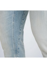 Krupan plan svijetloplavih traperica s detaljem kontrastnog šava koji se proteže niz unutarnju stranu bedra.