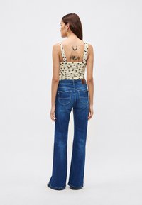 Kék farmer, bővülő szárú nadrág sima anyagból, krémszínű pöttyös, rövidített felsővel párosítva. Látható tetoválások a hátoldalon.