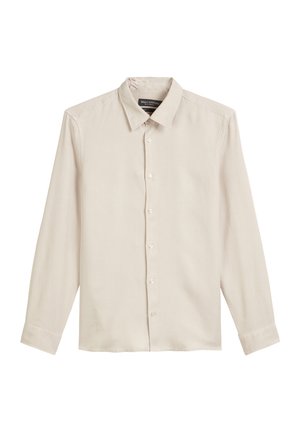 Chemise beige clair à manches longues en tissu lisse, avec un col classique, une fermeture à boutons et des poignets à boutons. Sans motifs ni accents.