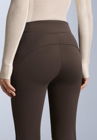 Hnědé legíny s vysokým pasem vyrobené z pružné tkaniny, s jemným švem a hladkou texturou, spárované se světlým ribbed svetrem.