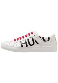 Baskets blanches en cuir avec une semelle plate, logo "HUGO" noir sur les côtés et lacets rouges, présentant une texture lisse et un design minimaliste.