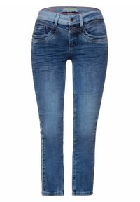 Modré džíny z denimu s úzkým střihem, které mají přední kapsy, zapínání na knoflík a zip, a mírné vyblednutí pro opotřebovaný vzhled.