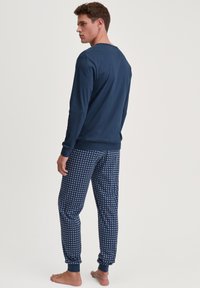 Marineblauwe top met lange mouwen en ronde hals, gecombineerd met pyjamabroek met een blauw geometrisch patroon en enkelsluitingen.