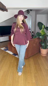 Μπορντό τοπ με φαρδιές μανίκες και σφιχτές πλευρές, ανοιχτό μπλε φαρδιά τζιν παντελόνια, λευκά πανέμορφα σανδάλια με τακούνι και ένα ταιριαστό καπέλο με φαρδύ γείσο. Φόντο ξύλινου δαπέδου.