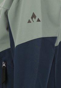 Vattentålig jacka med en ljusgrön övre del och en mörkblå nedre del. Har en geometrisk logotyp på axeln och dragkedjedetaljer.