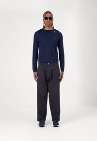 Navy long-sleeve shirt with a round neckline, paired with loose black trousers. Dark sports shoes, and round black sunglasses accent the look.