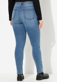 Pantalones de mezclilla azul con un diseño ajustado, que cuentan con una cinturilla alta, dos bolsillos traseros y una textura suave. Llevados con botas negras hasta el tobillo.