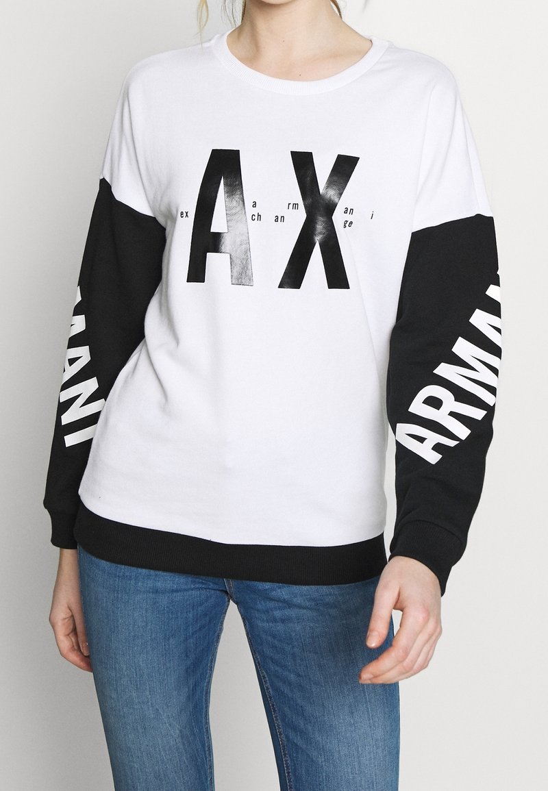 Weißer Sweatshirt mit schwarzen Ärmeln. Auf der Vorderseite prangt in fetten schwarzen Buchstaben "AX" und entlang des linken Ärmels steht "ARMANI". Baumwollstoff.