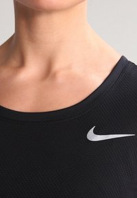 Musta urheilutoppi, jossa on tekstuuripinta, pyöreä kaula-aukko ja hopeinen Nike-logo vasemmalla puolella.