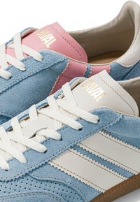 Paire de baskets de la marque CAVAL en daim bleu, bandes en cuir blanc, lacets blancs, et languettes roses et blanches avec lettres dorées.