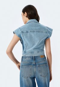 Giacca senza maniche in denim azzurro chiaro, con colletto strutturato, design corto e texture consumata. Abbinata a jeans a vita alta.
