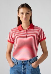 Polo à rayures rouges et blanches avec un col rouge, des manches courtes et un petit logo sur la poitrine, associé à un short en denim bleu taille haute.