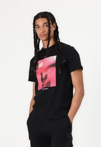 T-shirt en coton noir avec un graphique carré présentant un design abstrait rose et rouge. Manches courtes et coupe décontractée, sans matériel visible.