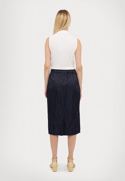 Navy knee-length skirt with a textured finish, elastic waistband, and a white sleeveless top. Footwear features block heels.