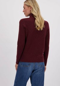 Bordeaux gebreide trui met een hoge hals. Heeft een ruitpatroon en geribbelde manchetten. Gecombineerd met lichtblauwe spijkerbroeken.