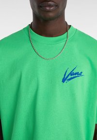 Zelené bavlněné tričko s modrým logem Vans na hrudi. Tkanina má hladkou texturu a uvolněný střih.