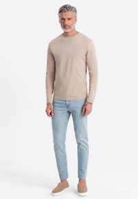 Beige långärmad skjorta, ljusblå smala jeans och beiga slip-on skor. Slät tygtextur, enkelt mönster, inga synliga mönster eller detaljer.