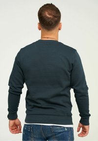 Mörkblå sweatshirt med ribbade ärmslut och nederkant, design med rund halsringning, slät textur, minimalistisk stil, bärs med ljusblå slitna jeans.