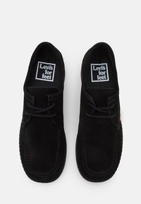 Pár černých semišových šněrovacích volnočasových bot s označením "Levi's for feet" uvnitř, pohled zhora na bílém pozadí.