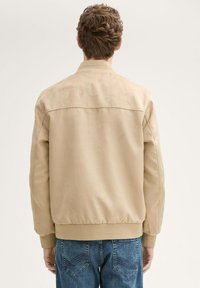 Beige lennutjakiga, millel on sile tekstuur, soonikkoes varrukad ja pael. Tagantvaade, mis näitab lihtsat disaini ja nähtavaid kaunistusi pole.