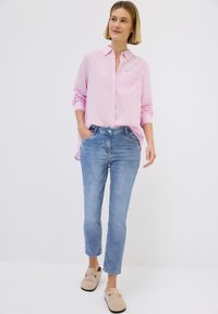 Chemise rayée rose avec une poche, associée à un jean bleu clair et des mocassins beiges. Présente une coupe décontractée, avec des manches retroussées et une texture subtile.