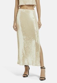 Beige rok met paillettenversiering, een zijsplit, een soepele textuur en een rechte silhouet. Gepaard met zwarte sierlijke hakken.