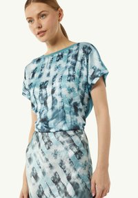 T-shirt z krótkim rękawem w niebiesko-czarnym wzorze tie-dye, charakteryzujący się luźnym krojem, miękkim materiałem i okrągłym dekoltem.