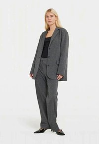 Fato cinza tecido, composto por um blazer de corte solto e calças combinando, apresentando um padrão texturizado e uma parte de cima preta elegante por baixo.