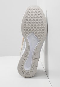 Vit atletisk skosula med texturerat greppmönster, som har en flexibel, gummibaserad yttersula och en centralt placerad Nike-logga.