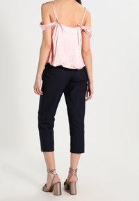 Ljust rosa satinblus med avfallna axlar och knytband, i kombination med marinblå cropped byxor och metalliska högklackade sandaler.