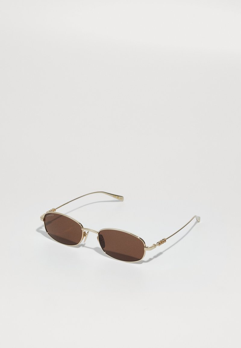 Gafas de sol metálicas doradas con lentes ovalados marrones. Patillas finas con acentos decorativos. Diseño elegante adecuado para diversas formas de rostro.