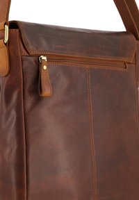 Hnědá kožená brašna přes rameno s kapsou na zip, robustním ramenním popruhem a viditelným prošitím. Hladký povrch s mírně opotřebovaným vzhledem.