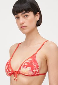 Top bikini rosso con design triangolare e motivi floreali dorati, con lacci regolabili al centro e spalline sottili. Texture opaca.