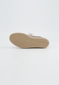 Beige Sneaker mit einer strukturierten Gummisohle, die kreisförmige Muster und ein geprägtes Markenlogo aufweist, leichtes Design und Schnürsenkel zur Befestigung.