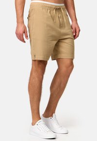 Bermudas beige hasta la rodilla, hechas de un tejido texturizado, con cintura elástica y cordón; cuenta con bolsillos laterales y dobladillo cosido.