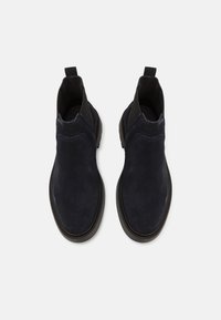 Tmavě námořnické semišové kotníkové boty s elastickými bočními panely, zaoblenou špičkou a texturovanou podrážkou. Obsahují poutko na patě pro snadné obouvání.